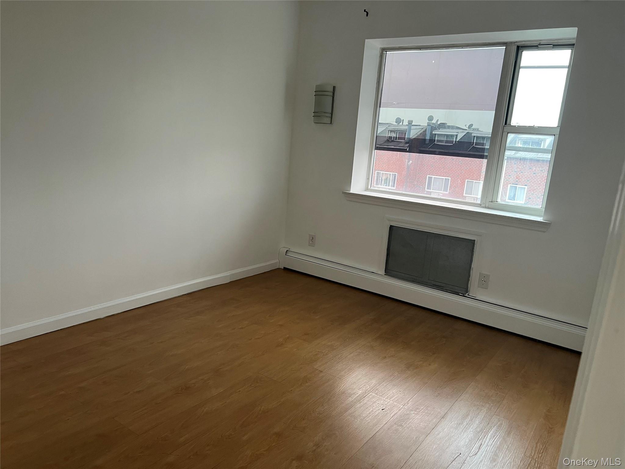 55-05 98th Street Queens, NY 11368 - Photo 5 of 12 Empty room featuring a baseboard radiator, wood finished floors, and baseboards