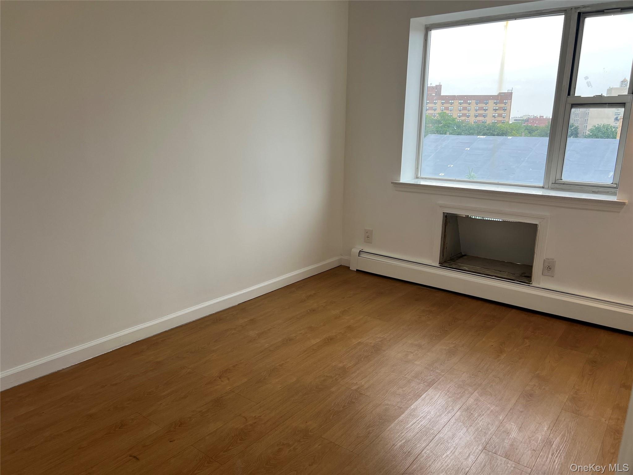 55-05 98th Street Queens, NY 11368 - Photo 10 of 12 Empty room featuring healthy amount of natural light, wood finished floors, a baseboard heating unit, and baseboards