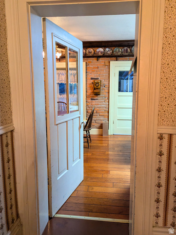 190 North 200 E Street Beaver, UT 84713 - Photo 21 of 40 Interior passage with a paneled door featuring glass inserts, wood-finish flooring, exposed brick wall, and decorative wallpaper