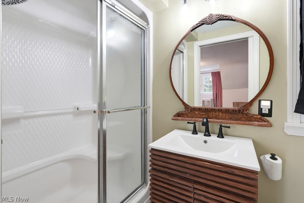 149 North Medina Line Road Akron, OH 44333 - Photo 14 of 42 Integrated shower and tub combination with glass enclosure, single vanity with wood-finish cabinetry, and a circular wall-mounted mirror
