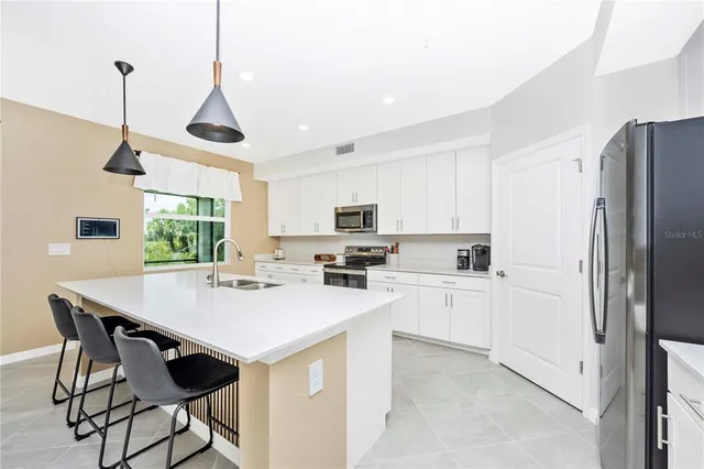 a kitchen with stainless steel appliances white cabinets a sink a stove a chimney a refrigerator and cabinets