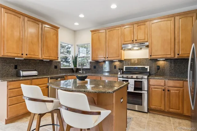 a kitchen with stainless steel appliances granite countertop a stove top oven a sink dishwasher a dining table and chairs with wooden floor