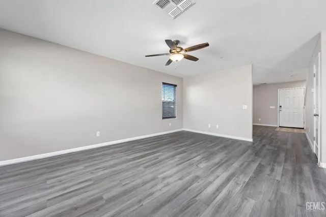 an empty room with wooden floor a ceiling fan kitchen view and a window