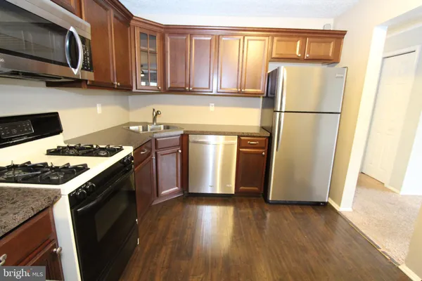 a kitchen with stainless steel appliances granite countertop a refrigerator a stove a sink dishwasher and wooden cabinets with wooden floor