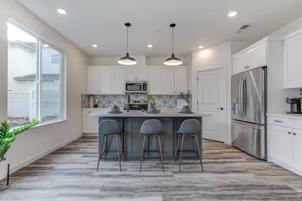 a kitchen with stainless steel appliances kitchen island granite countertop a refrigerator a stove a sink and white cabinets with wooden floor
