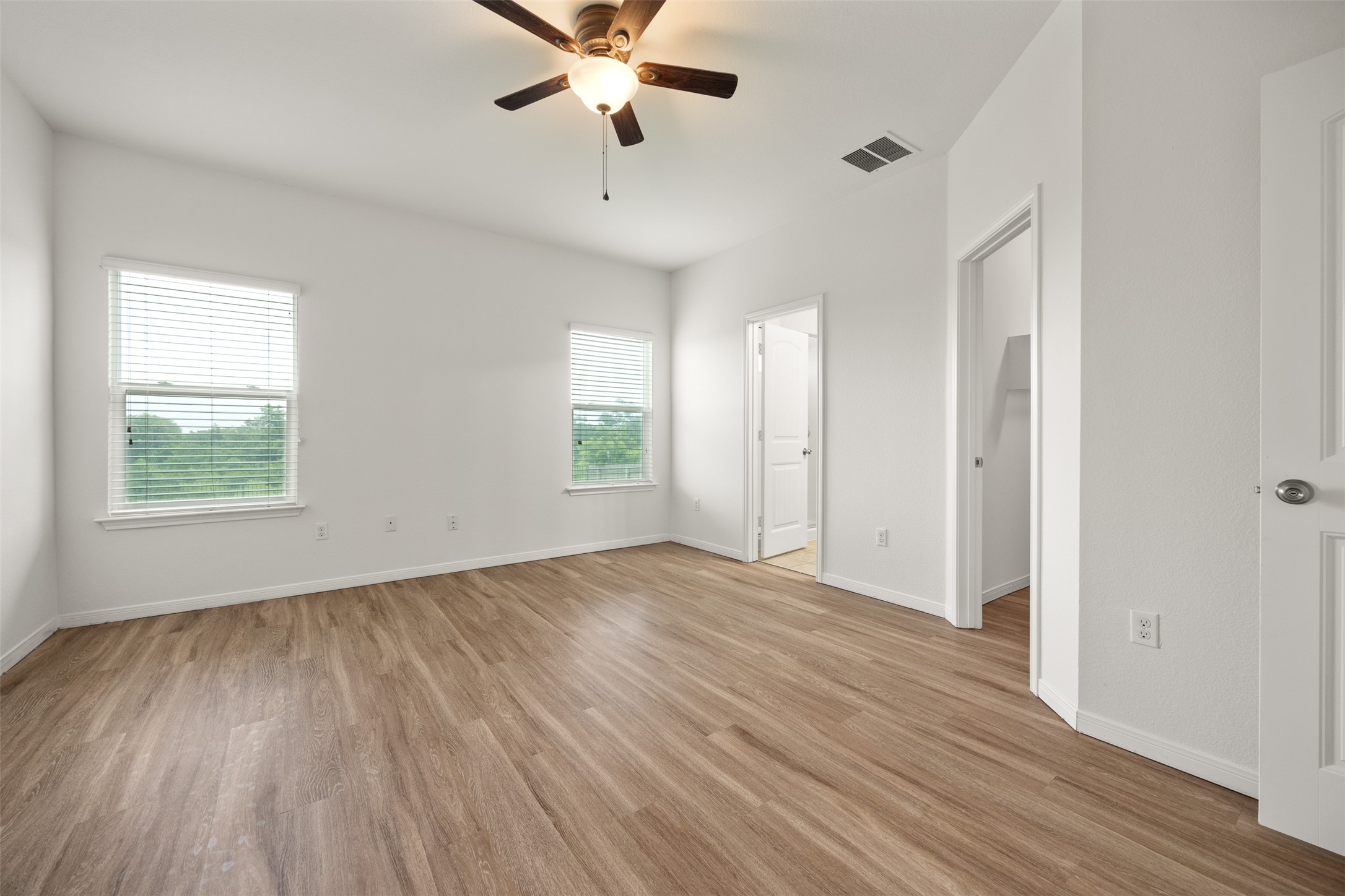 703 Liard River Road Hutto, TX 78634 - Photo 8 of 16 A well-lit primary bedroom featuring durable wood-look flooring and multiple windows, perfect for personalized decor.