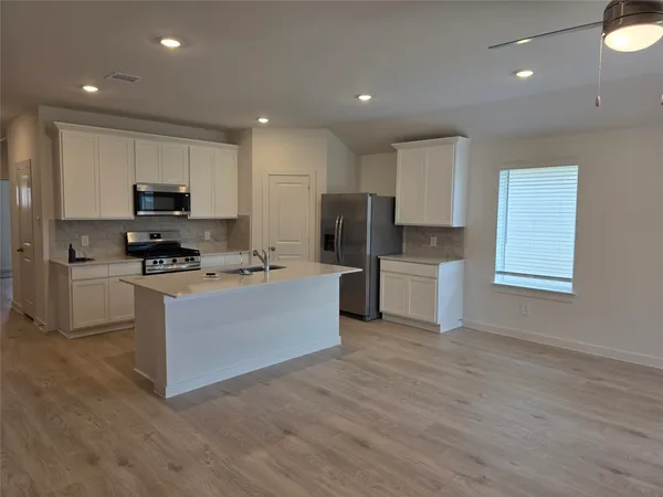 a kitchen with kitchen island granite countertop a stove top oven a sink a refrigerator and white cabinets with wooden floor