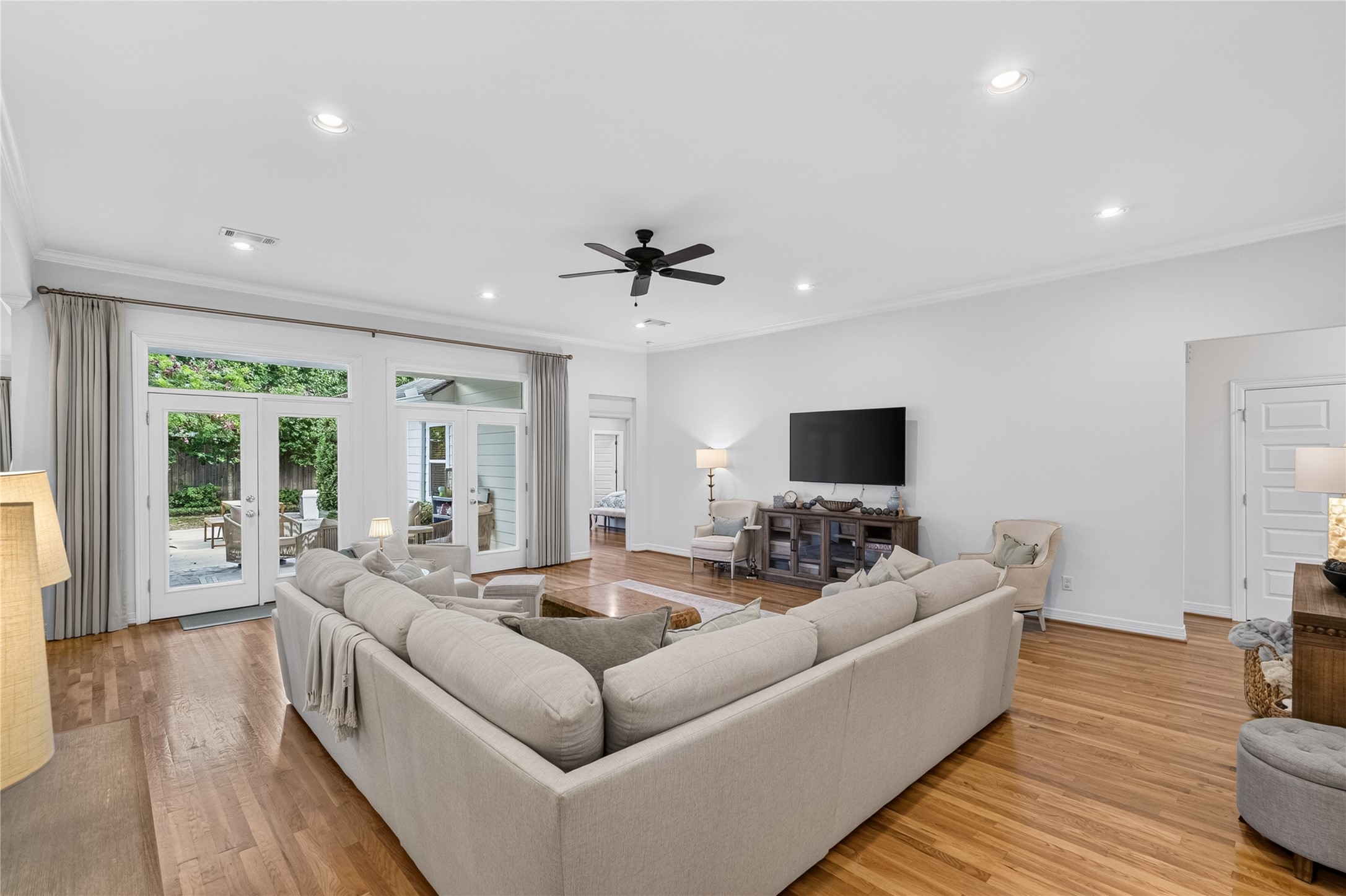Spacious living room with hardwood floors, a cozy sectional sofa, and abundant natural light from large windows and glass doors leading to the patio.
