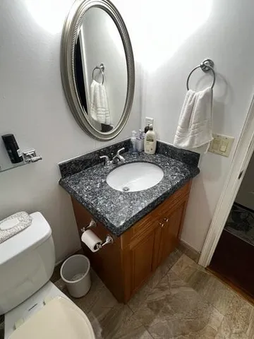 a bathroom with a granite countertop toilet a sink and a mirror