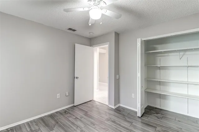 an empty room with wooden floor fan and windows
