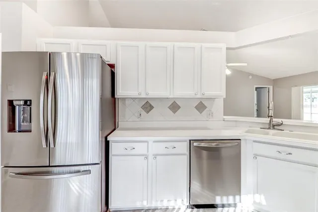 a kitchen with stainless steel appliances granite countertop a refrigerator a sink and white cabinets