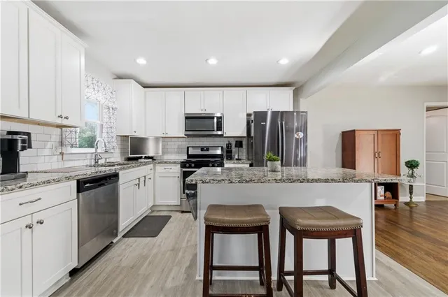 a kitchen with kitchen island granite countertop wooden floors white cabinets and stainless steel appliances