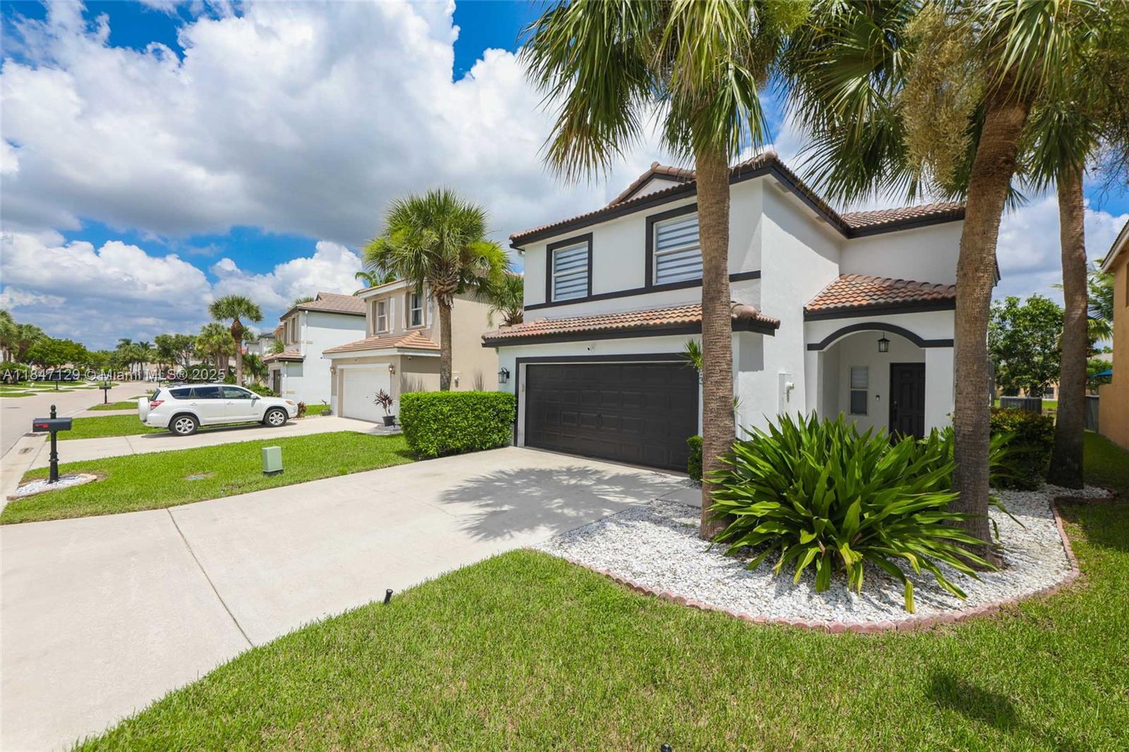 6073 Spring Isles Boulevard Lake Worth, FL 33463 - Photo 3 of 51 a view of a white house with a big yard and potted plants