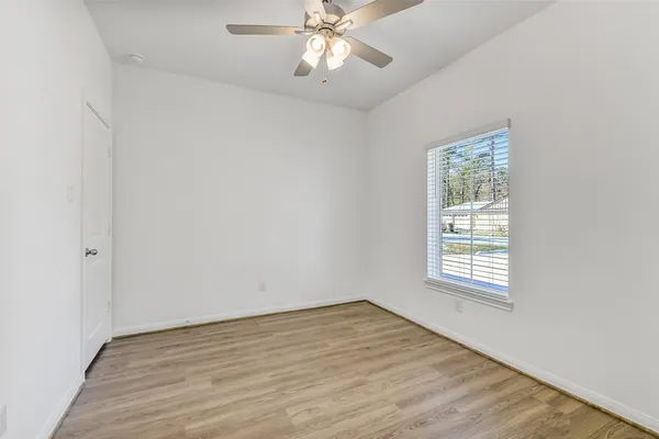 an empty room with wooden floor chandelier fan and windows