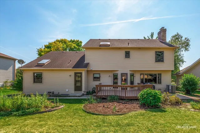 a house that is sitting in the grass with large trees and plants