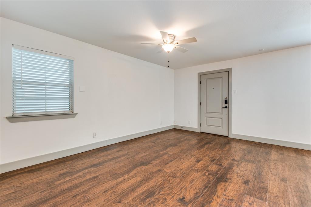 4633 Fairmount Street, Unit 109 Dallas, TX 75219 - Photo 13 of 14 Spacious room featuring wood-finish flooring, a light-colored entry door, and a ceiling fan with integrated lighting