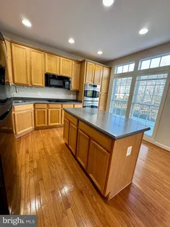 a kitchen with stainless steel appliances granite countertop wooden cabinets a sink a stove a refrigerator with grey cabinets and wooden floor