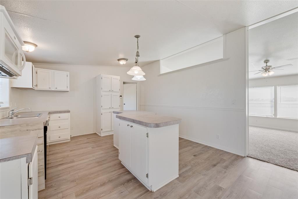 817 Kaufman Street Rosser, TX 75158 - Photo 12 of 29 Kitchen featuring white cabinets, decorative light fixtures, a center island, white microwave, and light countertops