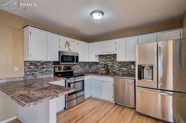 6773 Dale Road Colorado Springs, CO 80915 - Photo 12 of 45 Kitchen with a sink, appliances with stainless steel finishes, a peninsula, light wood-type flooring, and decorative backsplash