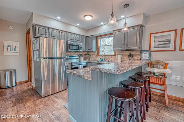 a kitchen with stainless steel appliances granite countertop a refrigerator a sink a stove and a dining table with wooden floor