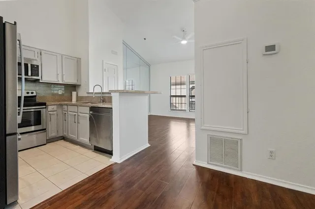 a kitchen with stainless steel appliances granite countertop a stove top oven a sink and white cabinets with wooden floor