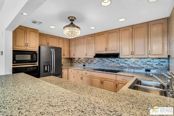 a kitchen with stainless steel appliances granite countertop a refrigerator a stove and a sink with wooden cabinets