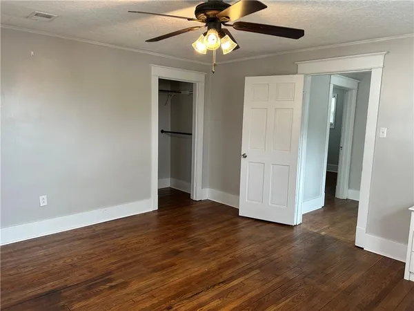 a view of an empty room with wooden floor and a ceiling fan