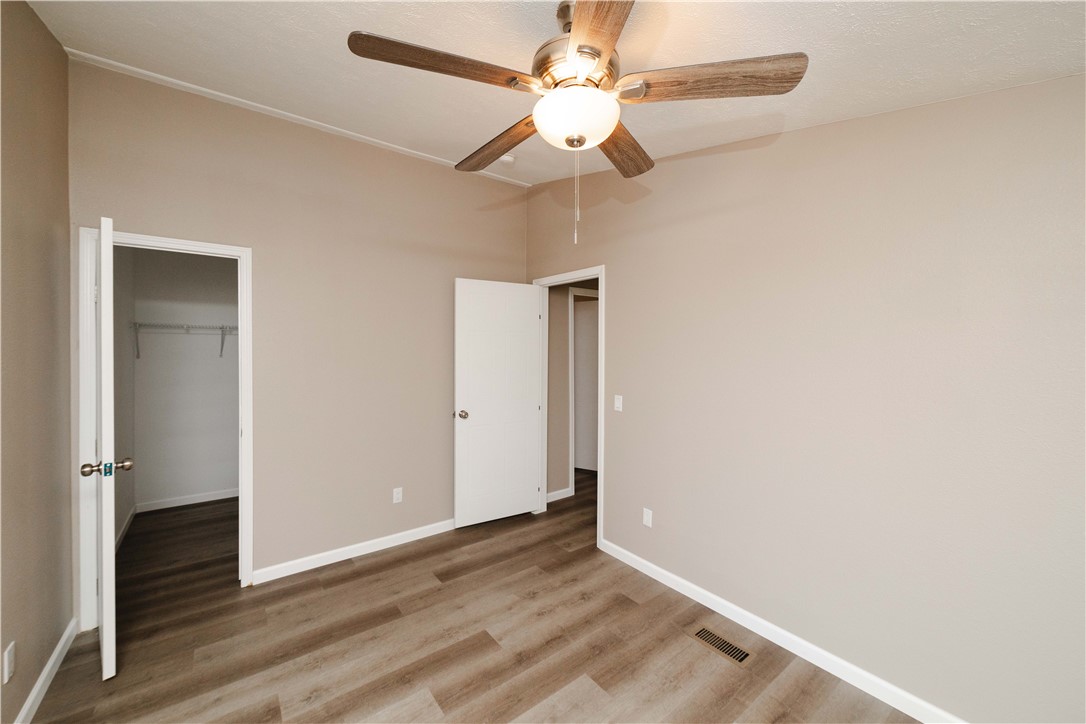 3248 West Carmichael Road Golden Valley, AZ 86413 - Photo 31 of 53 Unfurnished bedroom featuring a walk in closet, a ceiling fan, and light wood finished floors