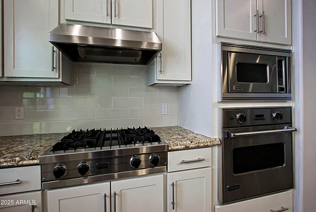 a kitchen with stainless steel appliances granite countertop white cabinets and black stove top oven with granite countertops