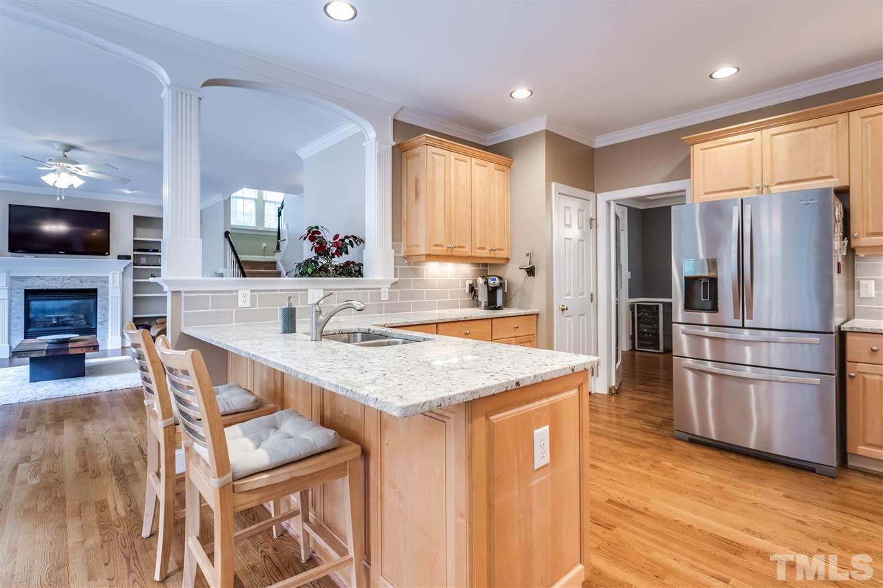 9428 Macon Road Raleigh, NC 27613 - Photo 10 of 25 a kitchen with kitchen island a stove a refrigerator a sink dishwasher with a fireplace and wooden floor