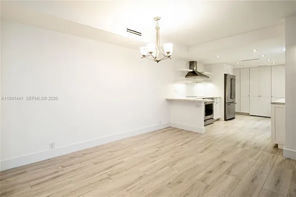 an empty room with wooden floor and kitchen view