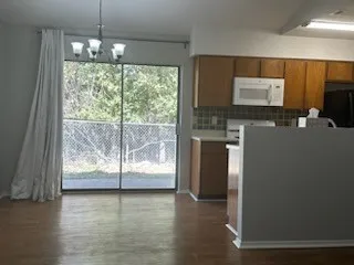 an empty room with wooden floor a ceiling fan and a kitchen view