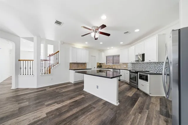a kitchen with stainless steel appliances granite countertop a stove top oven a sink dishwasher a refrigerator and white cabinets with wooden floor