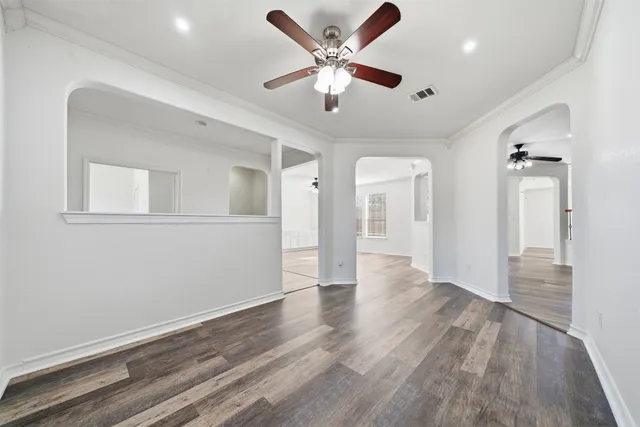 a view of an empty room with wooden floor and a ceiling fan