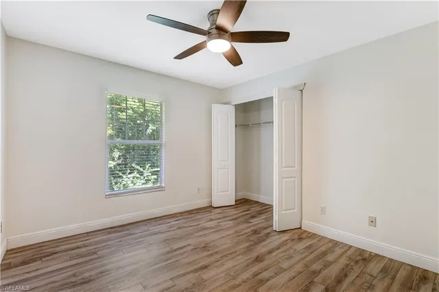 an empty room with wooden floor ceiling fan and windows