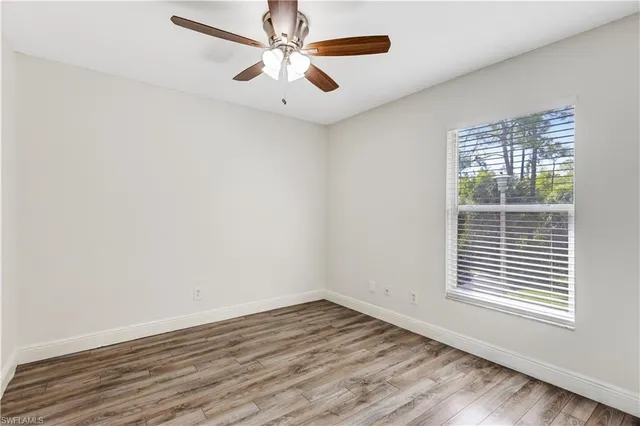an empty room with wooden floor chandelier fan and windows