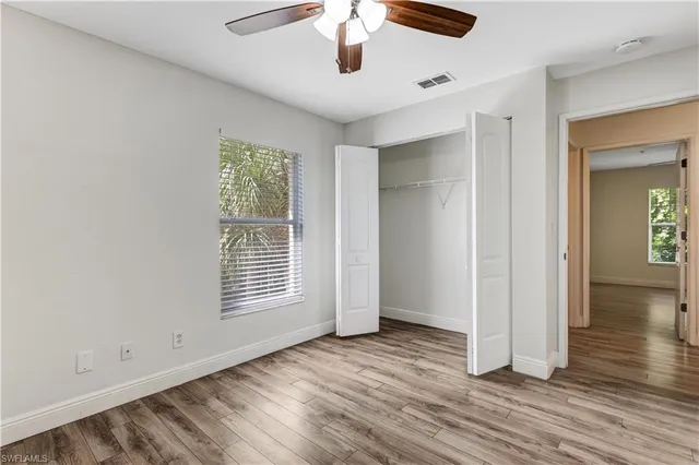 an empty room with wooden floor chandelier fan and windows