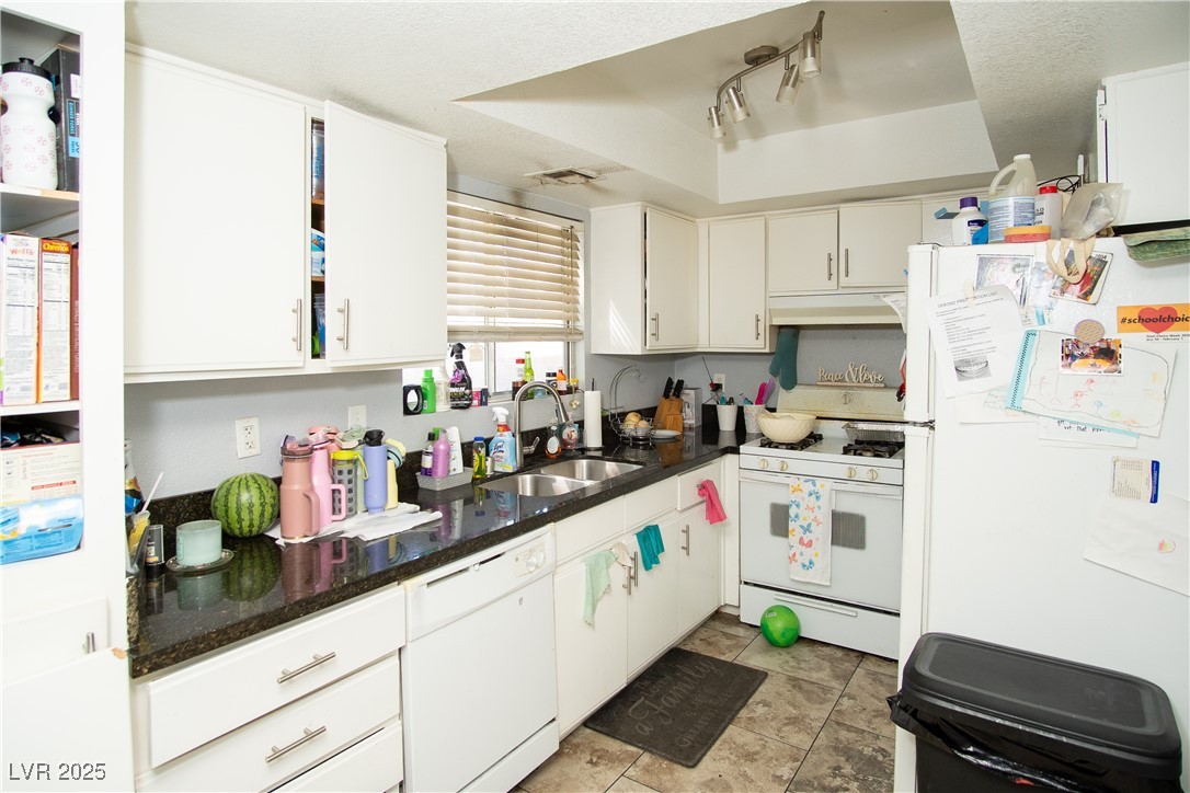 3844 Fitzpatrick Drive Las Vegas, NV 89115 - Photo 7 of 23 Kitchen with white appliances, white cabinetry, dark stone countertops, under cabinet range hood, and a textured ceiling