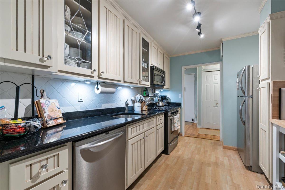 700 Shore Road, Unit 7Y Long Beach, NY 11561 - Photo 13 of 31 Kitchen featuring appliances with stainless steel finishes, glass insert cabinets, dark stone counters, decorative backsplash, and crown molding