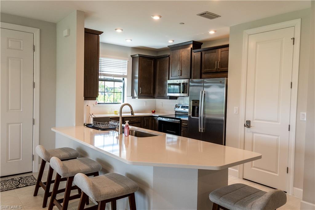 15335 Lucerna Street, Unit 104 Naples, FL 34114 - Photo 24 of 44 a kitchen with a table chairs refrigerator and microwave