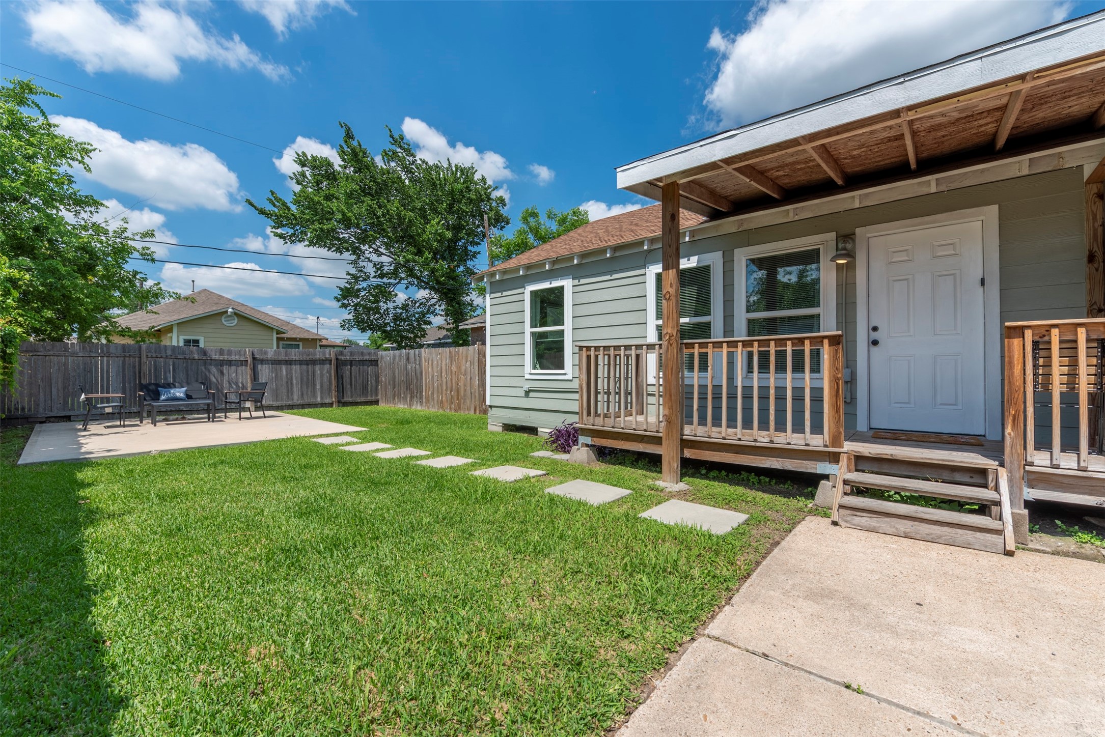 1121 Panama Street Houston, TX 77009 - Photo 1 of 35 Exterior view featuring fresh sage-green lap siding, white trim, oversized single-pane windows, covered wood-porch with pendant light, concrete stepping stone path, and fully fenced yard.