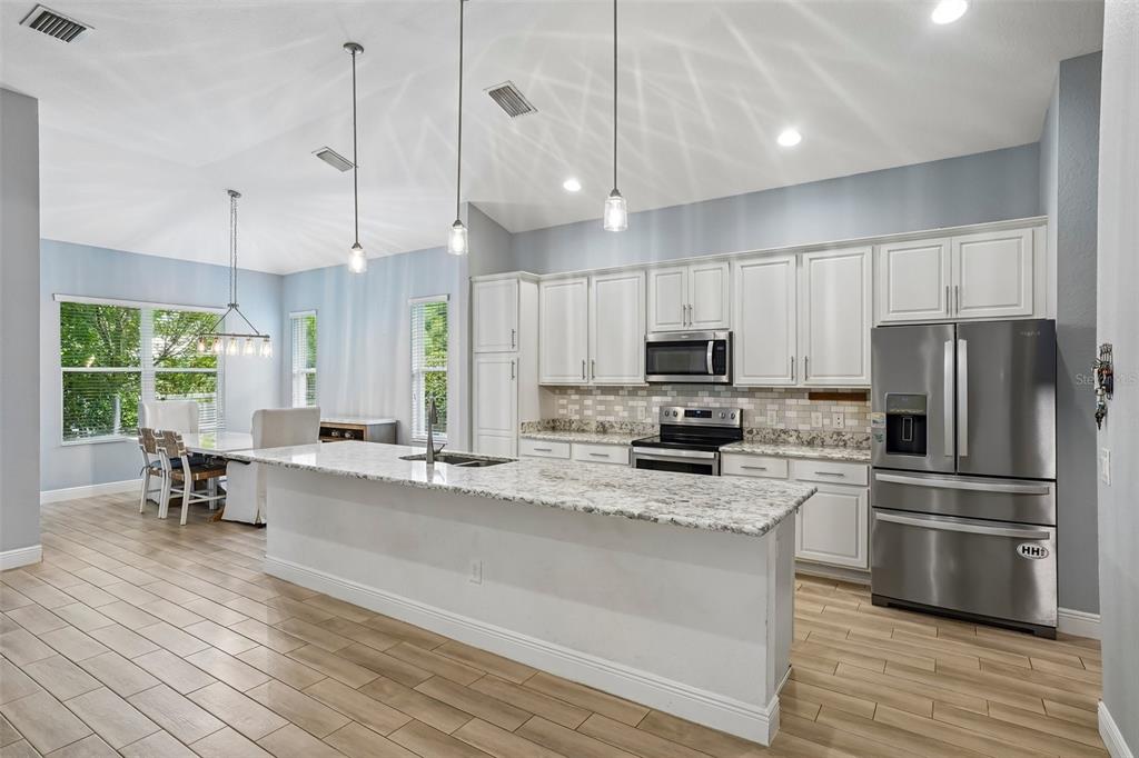 10339 Addison Shore Way Oxford, FL 34484 - Photo 35 of 54 a kitchen with stainless steel appliances kitchen island granite countertop a refrigerator a stove a microwave oven a sink with island and chairs with wooden floor