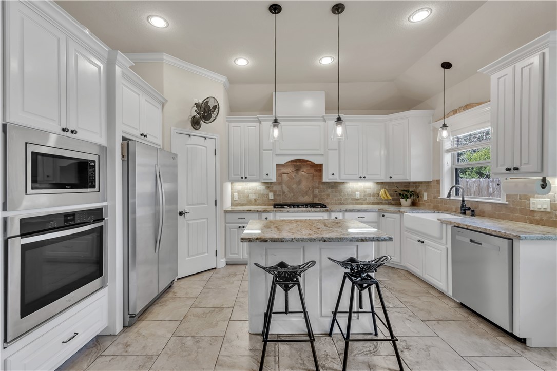 8312 Raintree Drive College Station, TX 77845 - Photo 9 of 30 Kitchen featuring white cabinetry, stone-finish countertops, stainless steel appliances, a center island with seating, and tile flooring