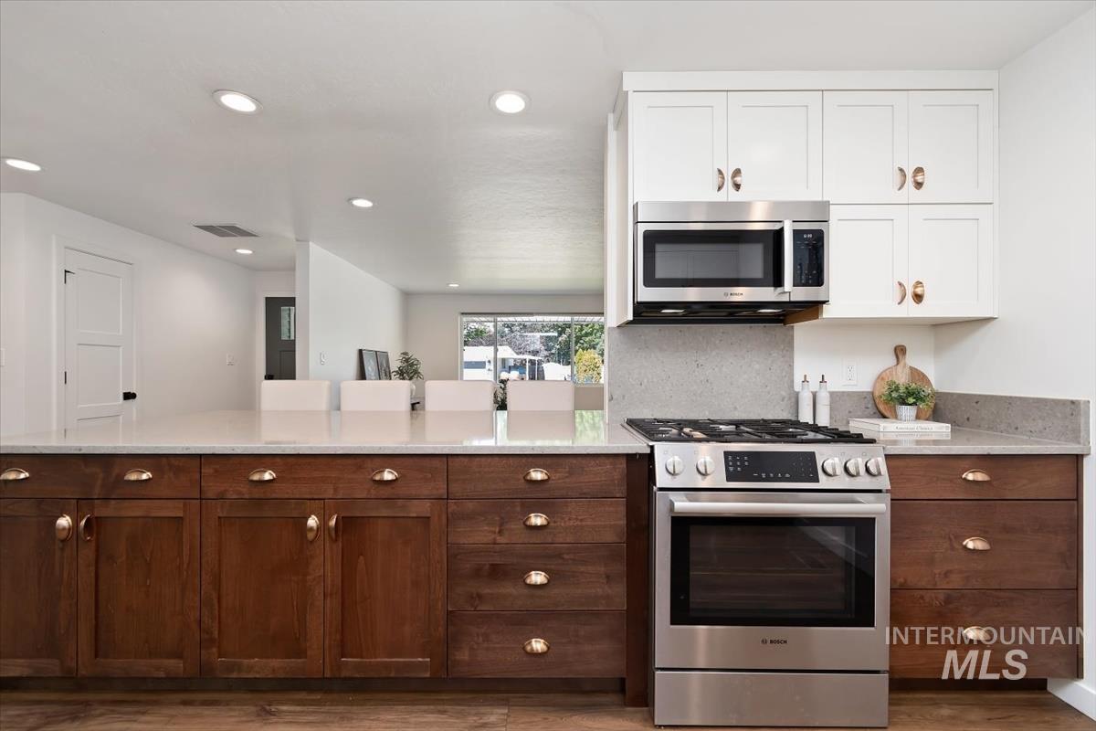 2217 North Middlefield Road Boise, ID 83704 - Photo 14 of 34 Gourmet kitchen featuring a built-in stainless steel microwave, gas range, wood-finish lower cabinetry, white upper cabinetry, and a light-toned countertop