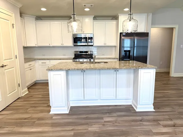 a kitchen with stainless steel appliances kitchen island granite countertop a refrigerator a stove and a sink with wooden floor