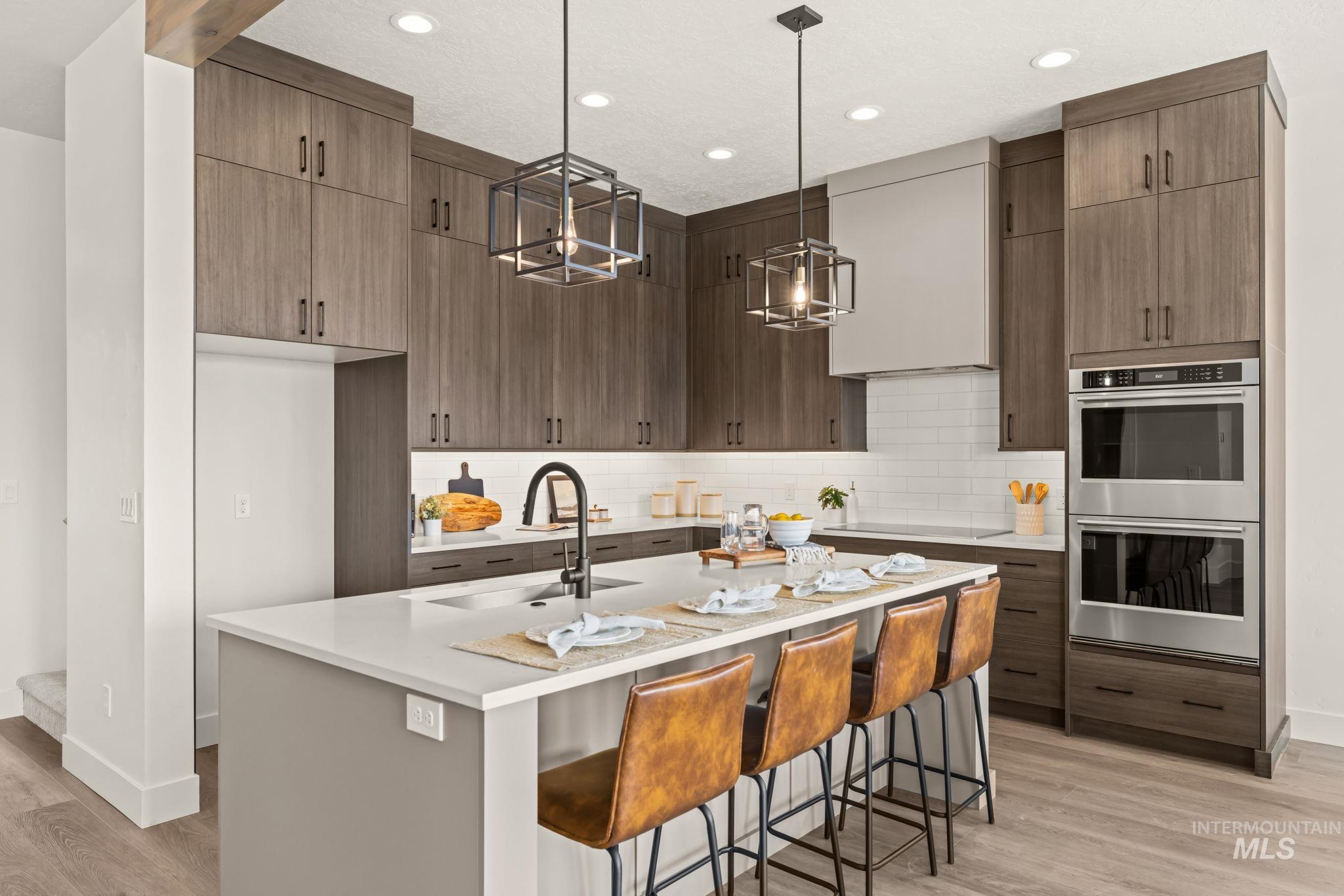 345 South Strut Way Boise, ID 83716 - Photo 6 of 50 Modern kitchen featuring wood-finish cabinetry, a large kitchen island with counter seating, stainless steel double wall ovens, a tile backsplash, and recessed lighting