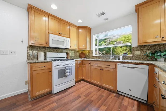 a kitchen with stainless steel appliances granite countertop wooden cabinets a sink a stove a refrigerator with grey cabinets and wooden floor