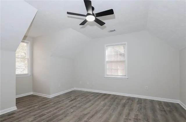 an empty room with wooden floor ceiling fan and windows