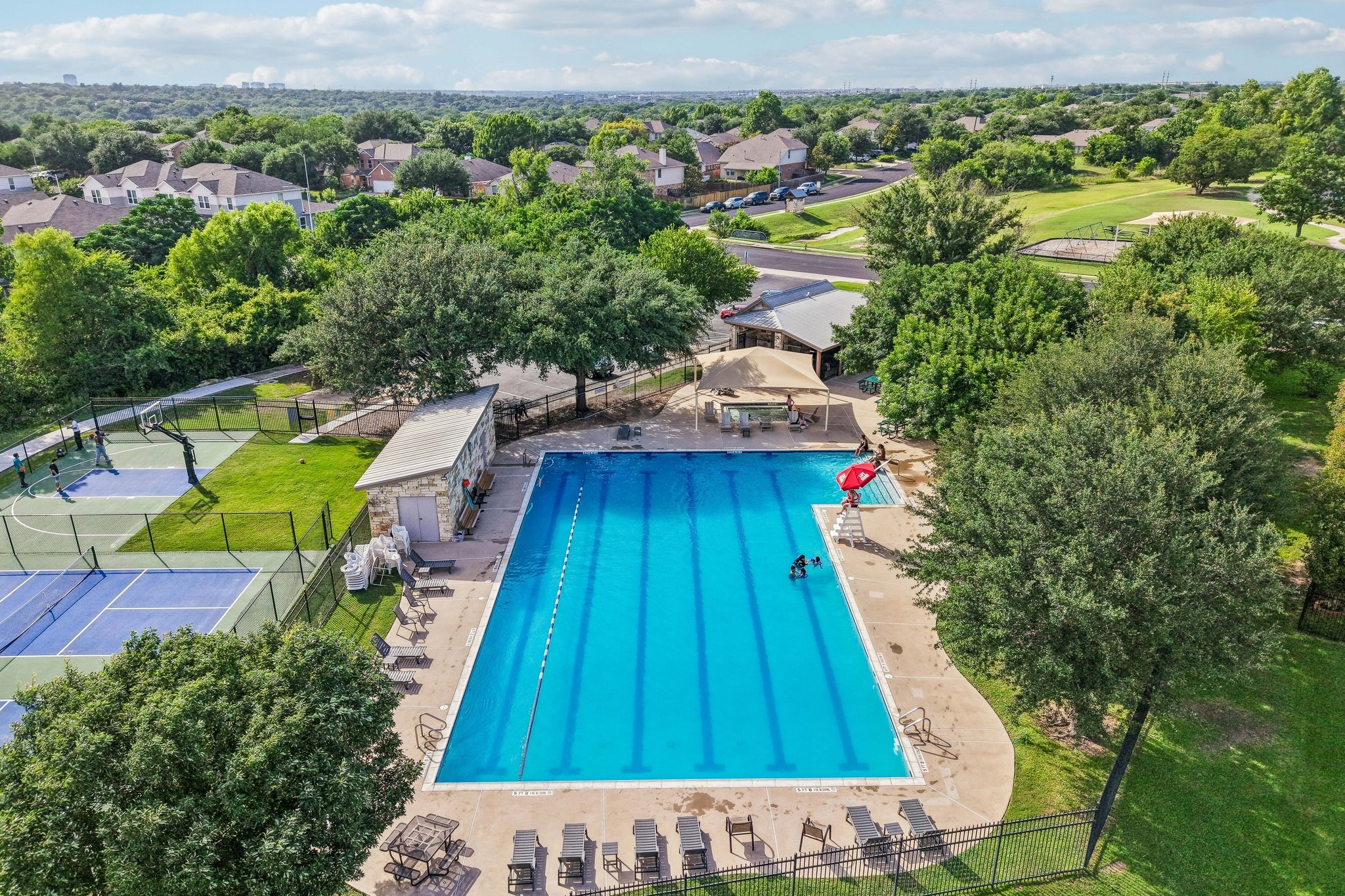 1721 Long Rifle Drive Austin, TX 78754 - Photo 37 of 38 An aerial perspective reveals a vibrant community pool with adjacent tennis and basketball courts, nestled among lush greenery.