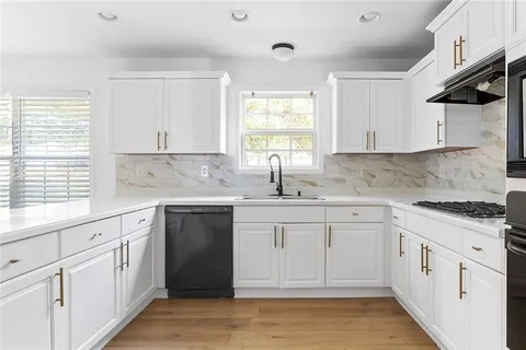 a kitchen with white cabinets appliances a sink and a window